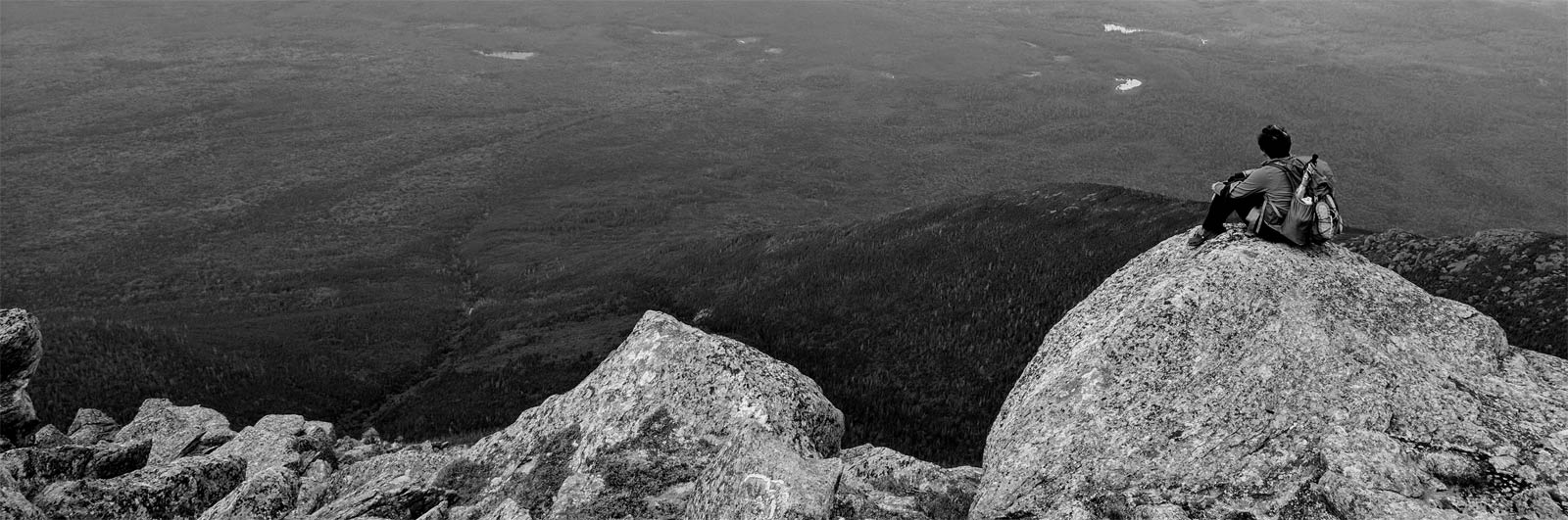 Woman with backpack sitting down and looking out over valley