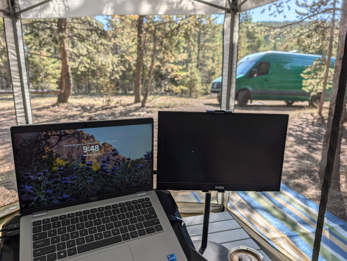 Dual monitors at a workstation in a shade canopy in the forest with a green van in the background