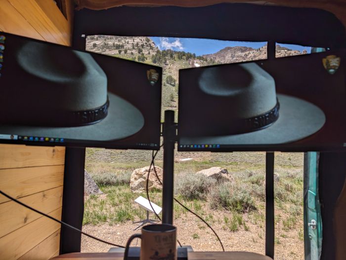 Dual monitors at a workstation in a campervan with views of mountains and a Starlink dish