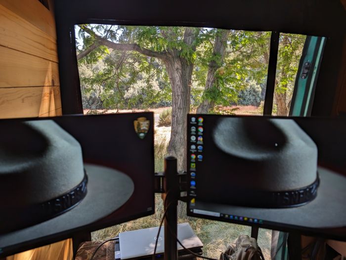 Dual monitors at a workstation in a campervan with views of deciduous trees