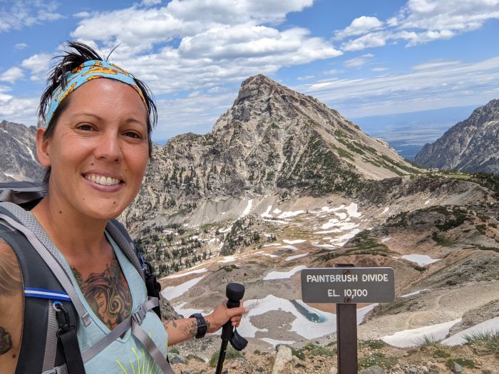 A woman holding a trekking pole with a mountain in the background and traces of snow