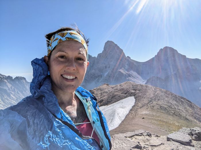 A woman wearing running gear with the Grand Tetons and bit of snow in the background
