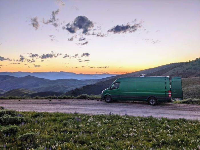 Green van overlooking mountains in the background with whispy clouds in the sky