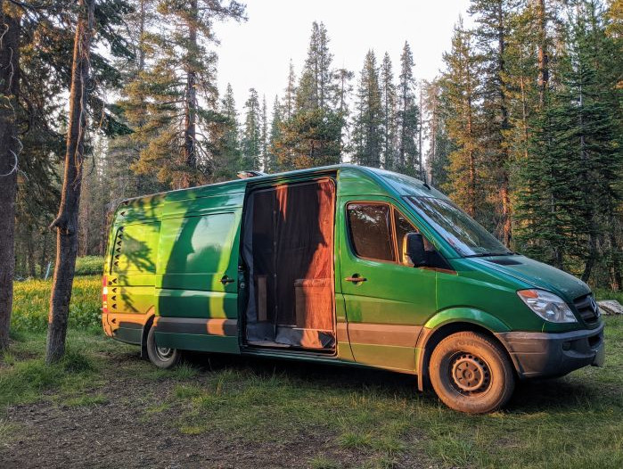 Green van in the golden sunlight with the slider open in a conifer forest