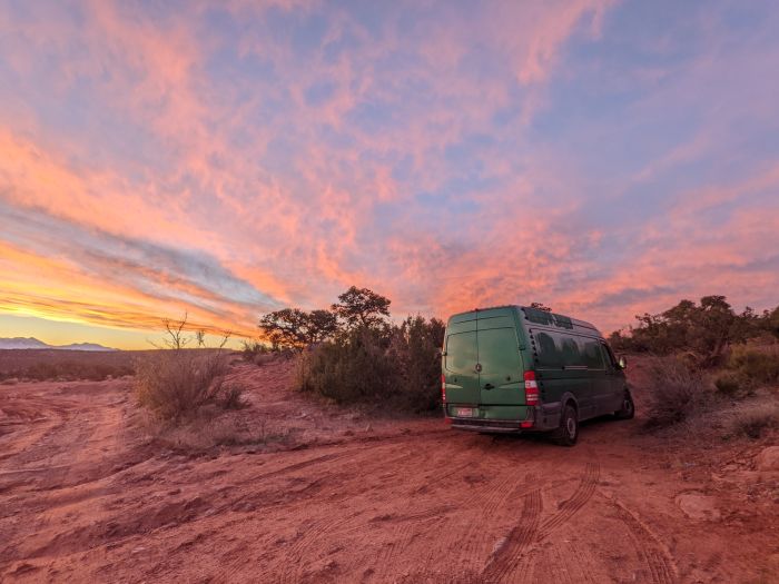 Green van in a red desert as the sun rises with peach and pink clouds in a blue sky